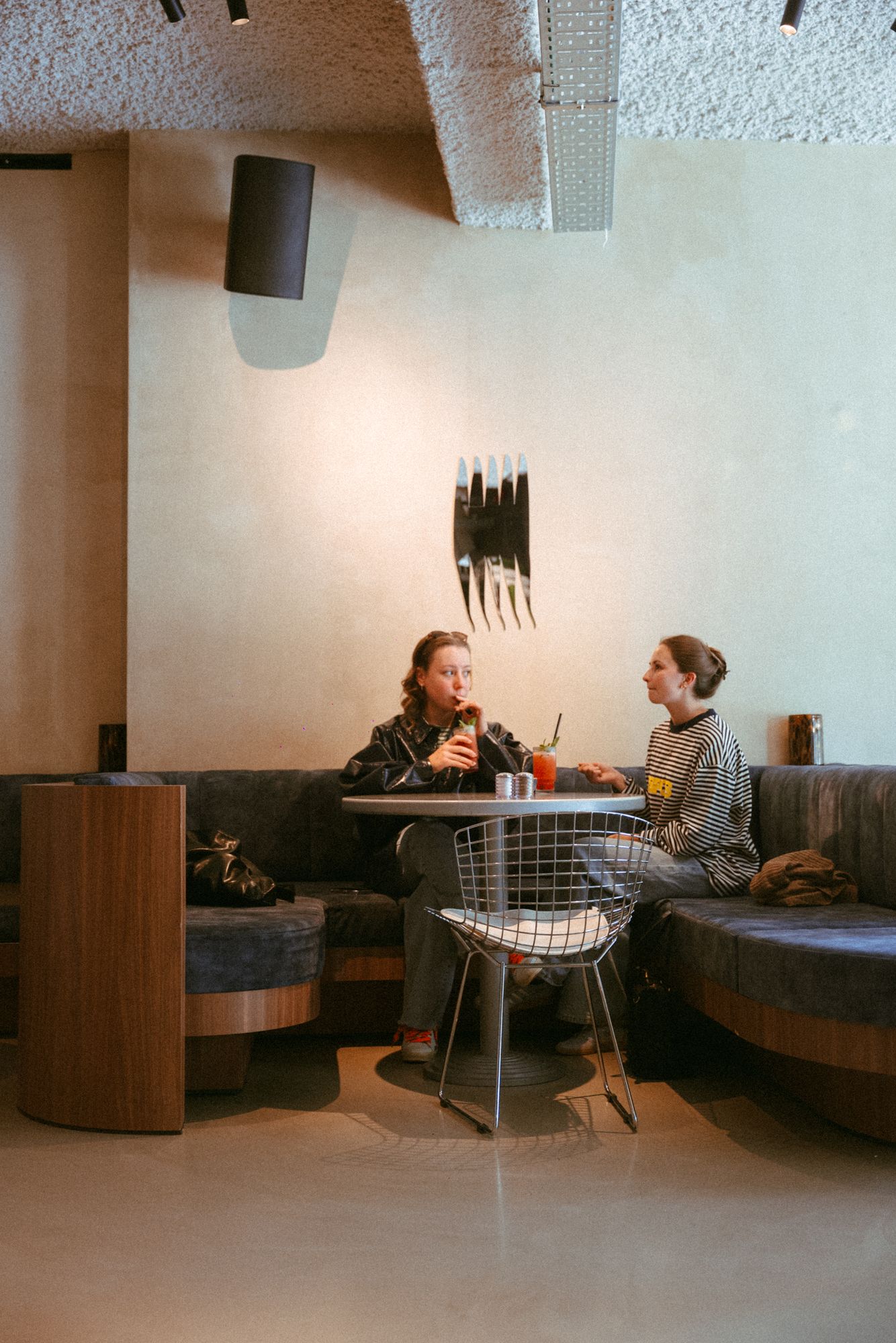 Two friends with drinks in the booth under the Claw sculpture